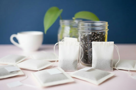 Glass jar with black tea leaves on a white surface with green leaves in the background