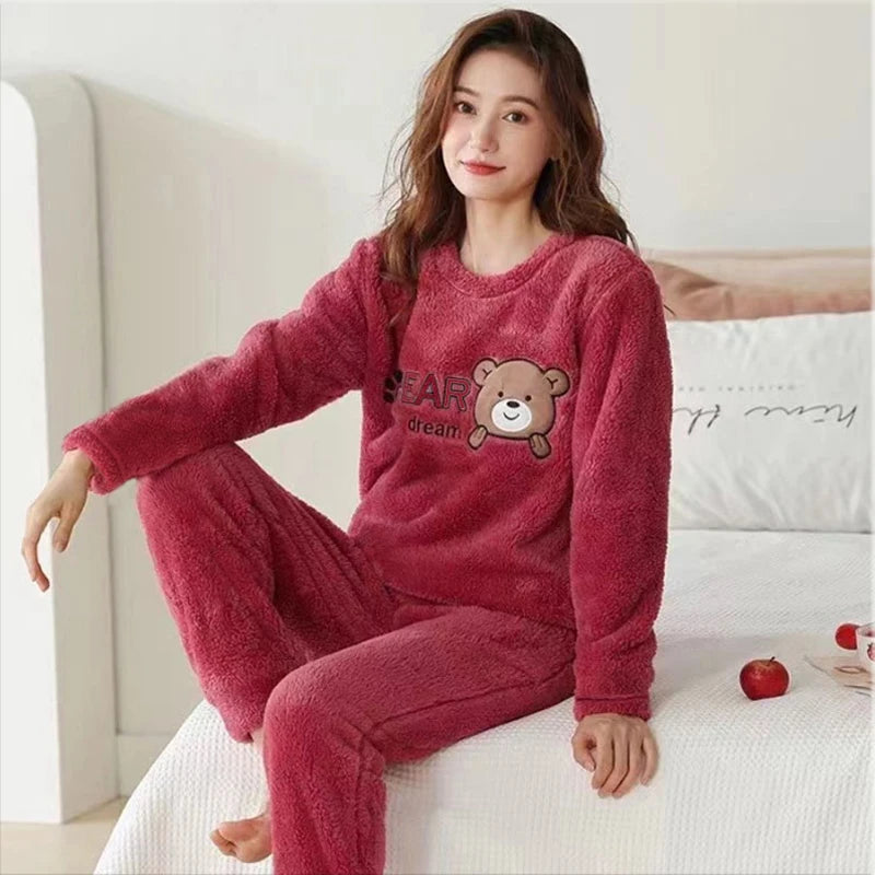 Woman wearing a pink fleece pajama set with a bear design on a bed.