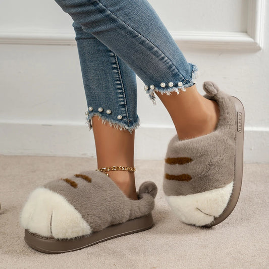 Gray fuzzy slippers with brown accents worn indoors on a carpeted floor.